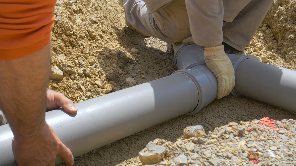 Installation de Tuyaux PVC pour Assainissement sur Chantier Installation de tuyaux PVC gris par deux ouvriers sur un chantier d'assainissement en tranchée sablonneuse.