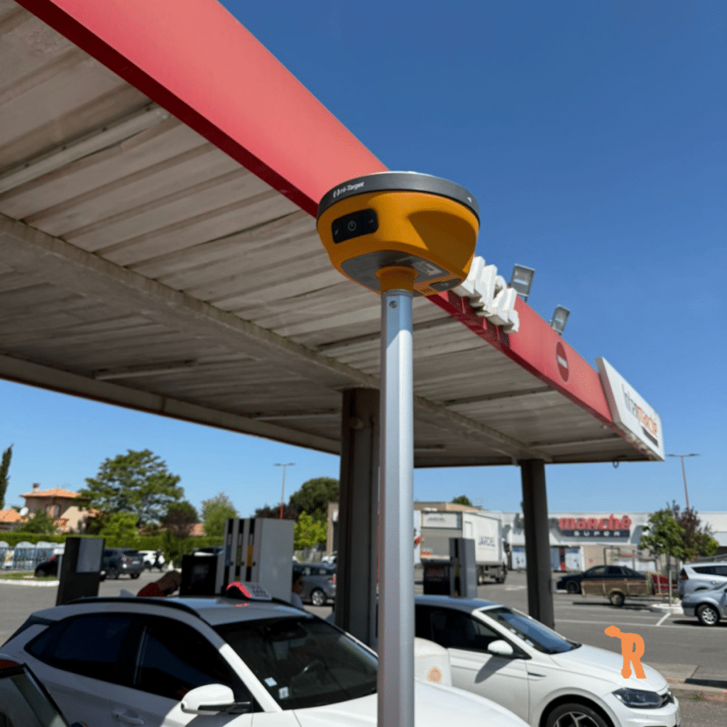 Récepteur GNSS Hi-Target : Topographie Haute Précision Récepteur GNSS Hi-Target jaune sur canne de mesure devant un Intermarché, matériel de topographie haute précision.