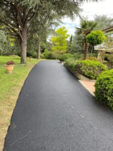 Allée en Enrobé Noir : Aménagement de Jardin Paysager Allée en enrobé noir bordée de verdure et d'arbres majestueux dans un jardin paysager.