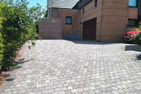 Allée en pavés pour maison moderne | Aménagement extérieur Allée de garage pavée en pavés gris devant une maison moderne en briques sous un ciel ensoleillé.