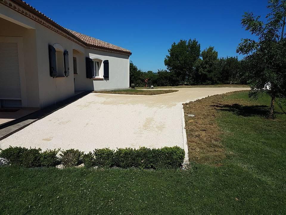 Allée en gravier et aménagement extérieur de maison Allée de gravier stabilisé devant une maison moderne avec volets sombres et jardin verdoyant sous un ciel bleu.