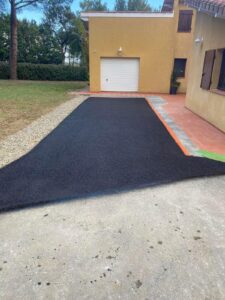 Enrobé noir pour une allée de garage moderne et propre Allée en bitume noir neuf devant un garage de maison, bordée de graviers et d'un trottoir carrelé.