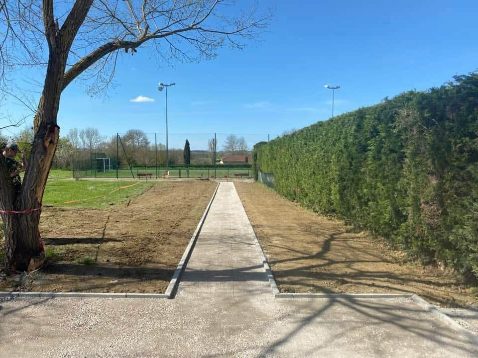 Aménagement d'une allée de jardin en gravier avec bordures Allée de jardin en gravier avec bordures en pierre, terrassement en cours vers un terrain de sport extérieur.
