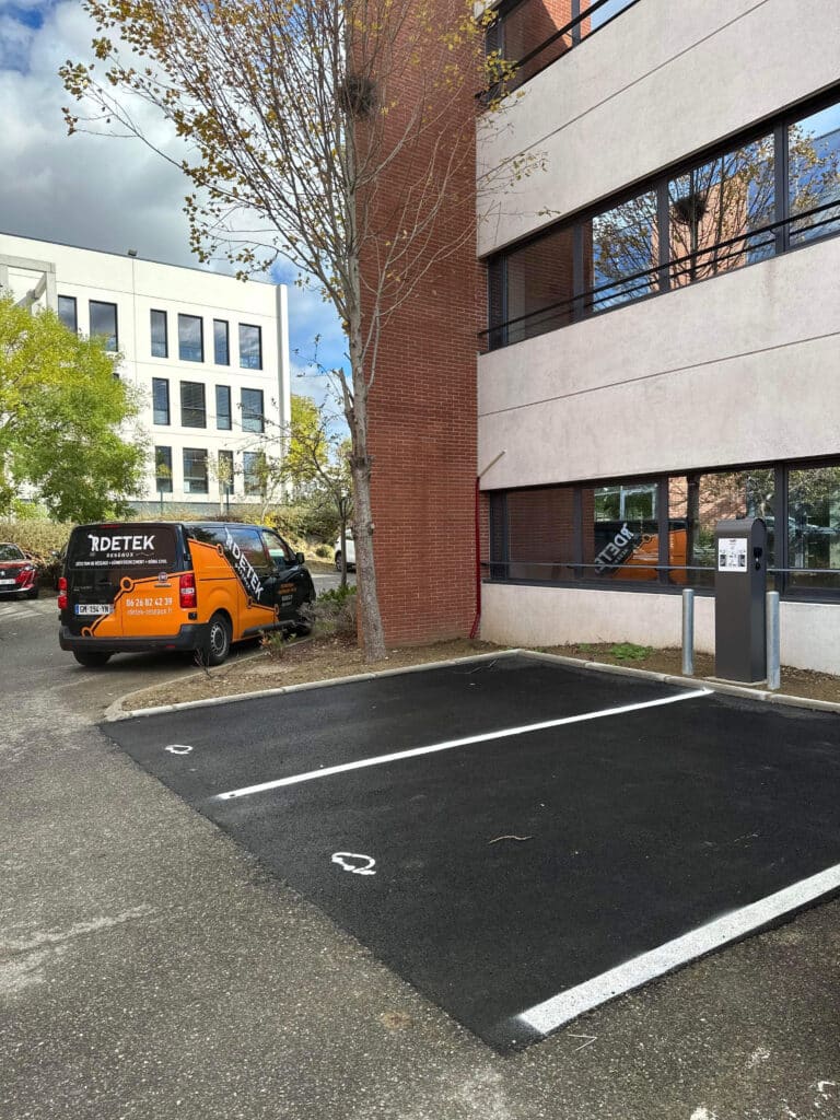 Borne de recharge et parking électrique RDETEK RÉSEAUX Fourgon RDETEK RÉSEAUX devant des places de parking pour véhicules électriques avec borne de recharge.