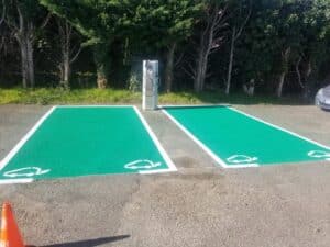 Borne de recharge électrique : deux places de parking vertes Deux places de parking vertes avec bornes de recharge pour voitures électriques devant une rangée d'arbres.