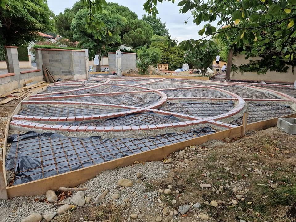 Dalle béton décorative : préparation et motifs en briques Préparation d'une dalle béton avec ferraillage et motifs circulaires en briques pour un aménagement paysager extérieur.