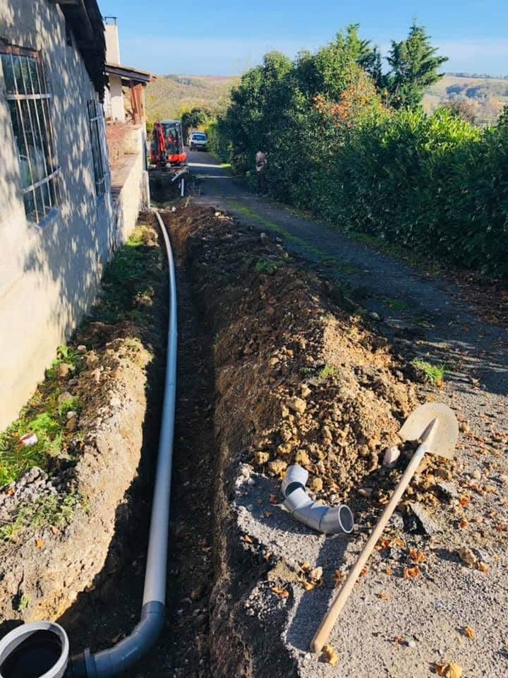 Drainage de Maison : Pose de Tuyaux PVC en Tranchée Pose de tuyau de canalisation dans une tranchée le long d'un bâtiment, avec pelle et tas de terre à proximité.