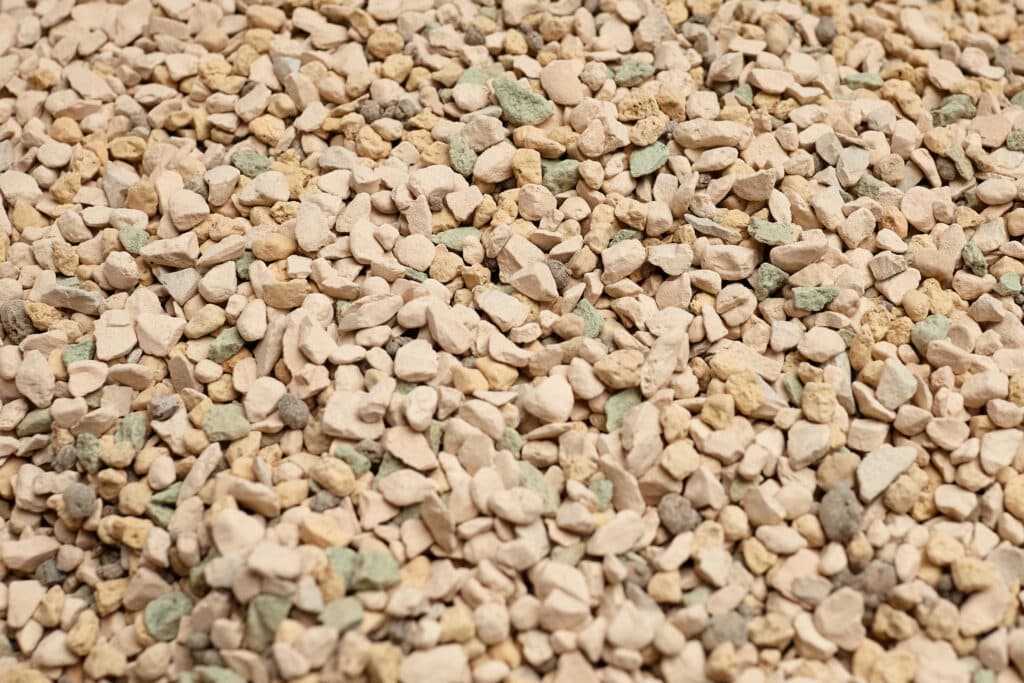 Gros plan sur des granulés de litière minérale pour chat beige, vert et gris à texture poreuse et absorbante.