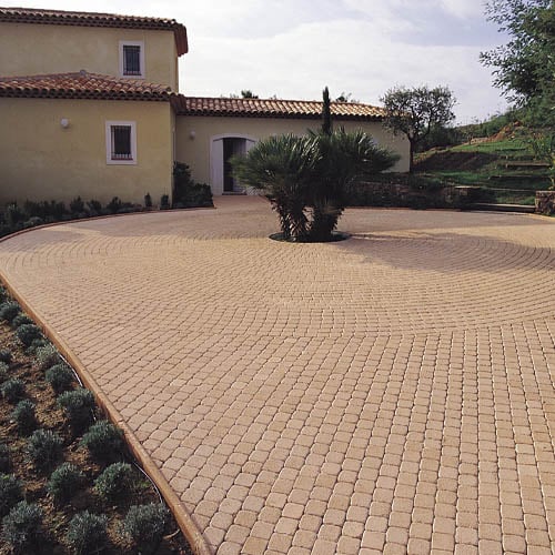 Pavage d'allée décoratif en spirale pour villa de luxe Allée en pavés beiges posés en spirale autour d'un palmier devant une villa de style méditerranéen.