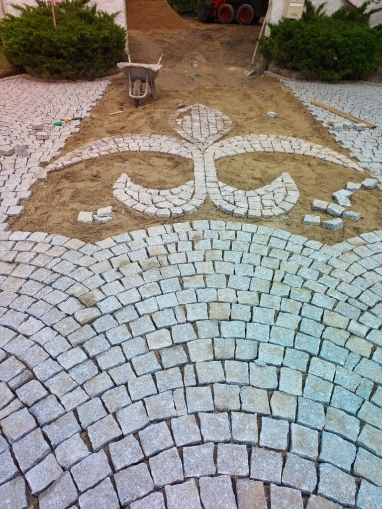 Pavage Décoratif en Pierre Naturelle : Motif Fleur de Lys Pose de pavés en granit formant un motif de fleur de lys sur un lit de sable pour une allée de jardin décorative.