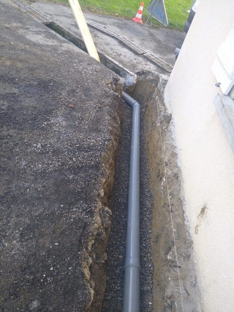 Pose de tuyau PVC d'évacuation dans une tranchée de gravier Pose d'un tuyau PVC gris sur gravier dans une tranchée de drainage le long d'une fondation de maison.