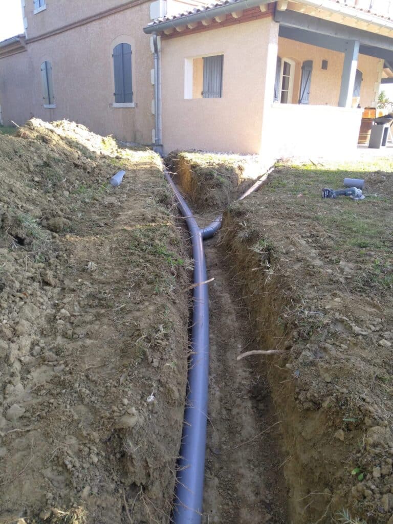 Drainage extérieur : pose de tuyaux PVC dans une tranchée Installation de tuyaux PVC gris pour évacuation des eaux pluviales dans une tranchée de jardin.