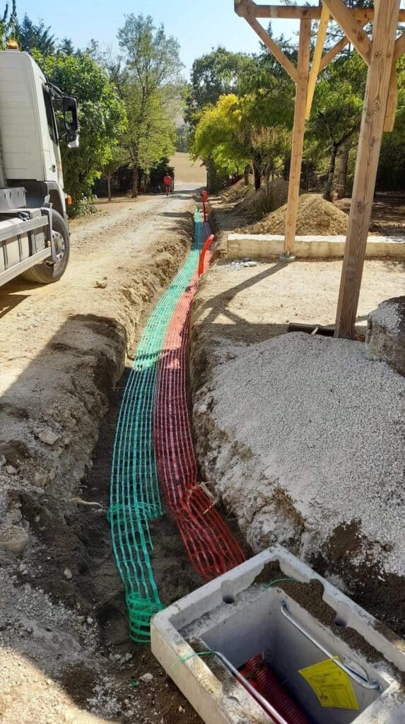 Pose de gaines et filets avertisseurs en tranchée de chantier Tranchée ouverte avec grillages avertisseurs rouge et vert pour réseaux enterrés et regard en béton sur un chantier.