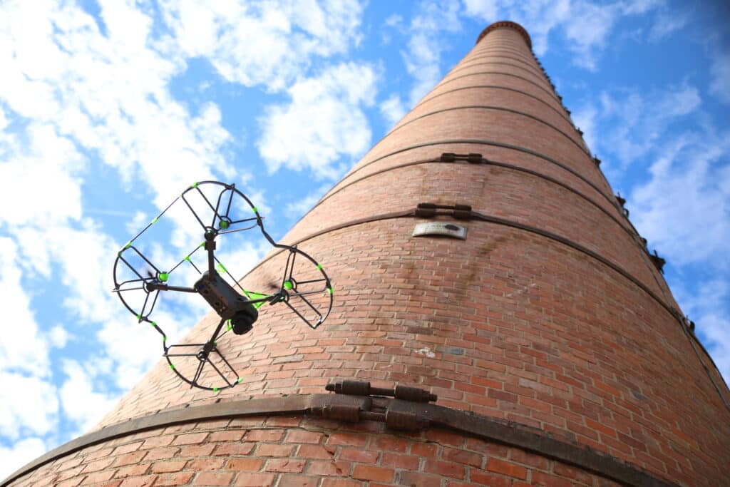 Inspection par drone d'une cheminée industrielle en brique Drone à protections vertes inspectant une cheminée en brique de Toulouse par temps clair.