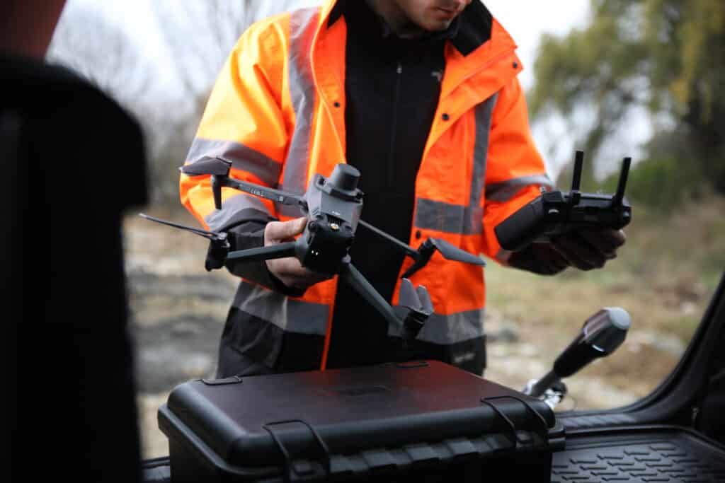Pilote de drone professionnel avec gilet de sécurité Pilote en veste haute visibilité orange tenant un drone professionnel et sa télécommande sur un site de travail.