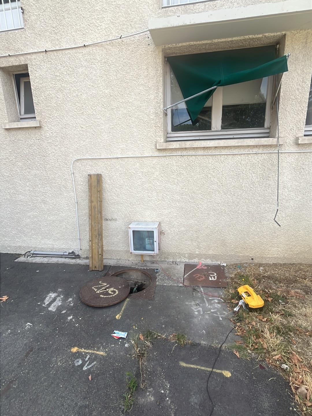 Détection de réseaux gaz et marquage au sol technique Regard GAZ ouvert, marquages au sol et détecteur jaune devant une façade d'immeuble avec coffret technique.